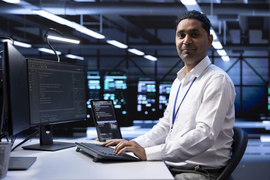 A smiling IT expert sitting at a desk with a computer